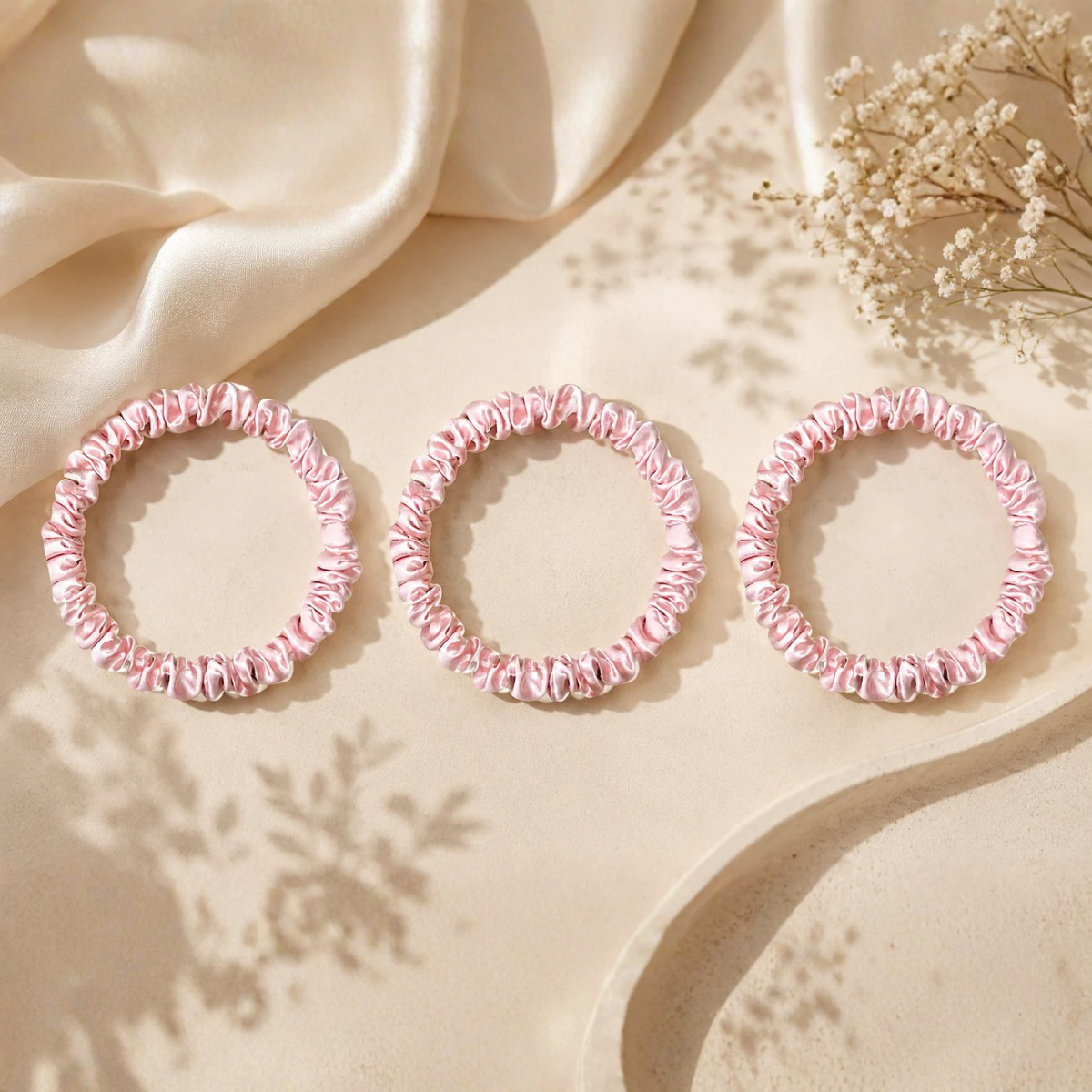 Pink 22 momme silk scrunchies displayed on a luxury silk fabric background