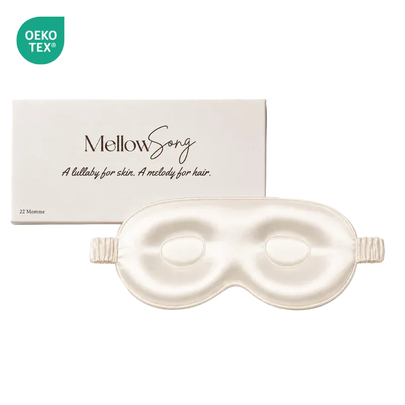 Cream-colored contoured silk eye mask by Mellow Song, displayed with its original white packaging box and an OEKO-TEX logo on a plain white background.